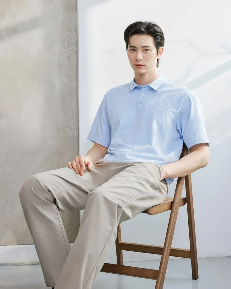 A man in a light blue striped polo sitting on a wooden chair
